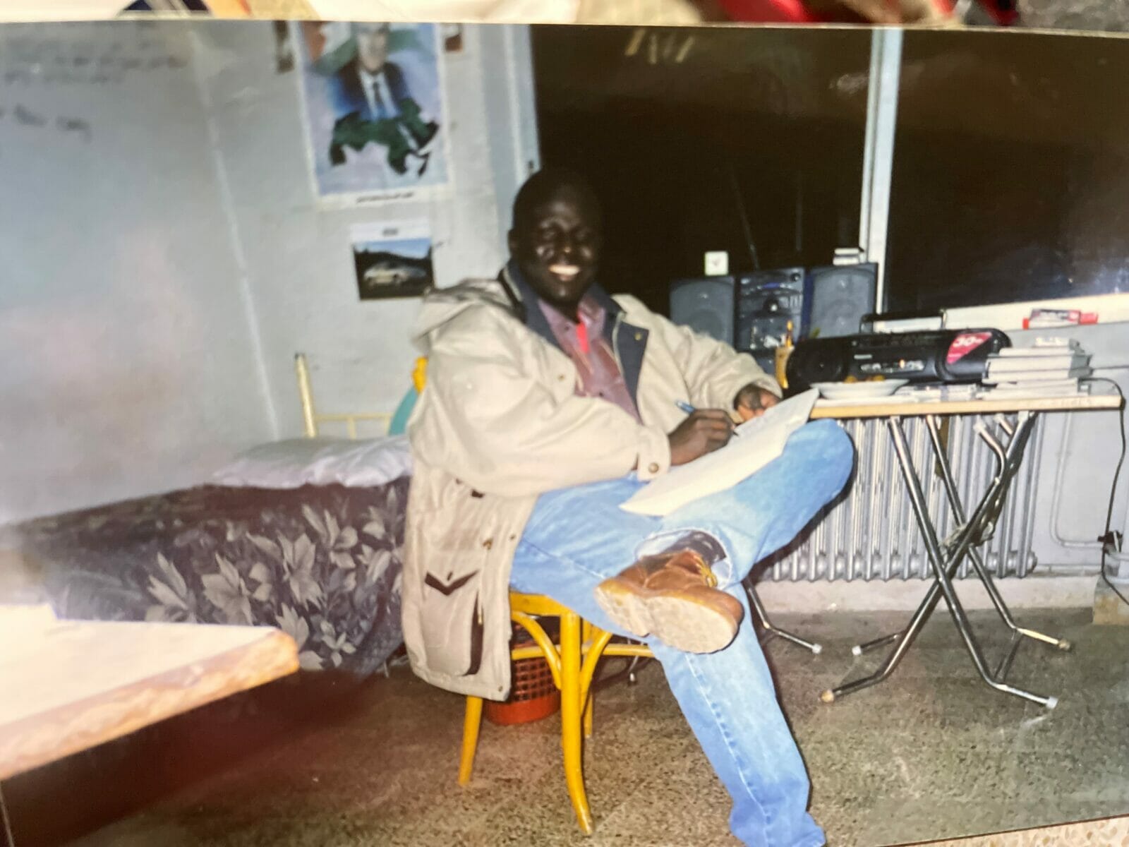 A young, 20-something-year-old student smiles at the camera in his dorm room in Damascus, Syria. At the time, Denis Kweri was living in a refugee camp. (Contributed