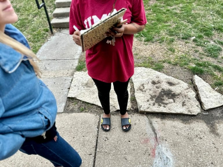 A woman in a red shirt holds a clipboard and signs a petition for her landlord to remedy lingering issues at Blue Valley Court Townhomes. 