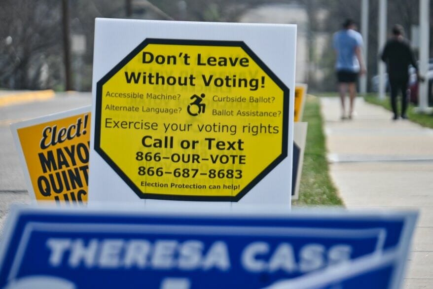 Pedestrians walk past a row of campaign and voter signs at Rockhurst University near a polling location on April 4, 2023 — the candidates who advanced from that election will be on the ballot June 20.