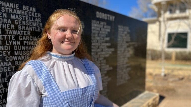 One of the museum's Dorothy Gale tour guides stands in front of a monument etched with the names of the many Dorothys who have come before her at the Land of Oz in Liberal.