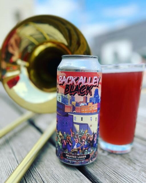 Double Shift’s new fruited lager Back Alley Black with a trombone in the background.