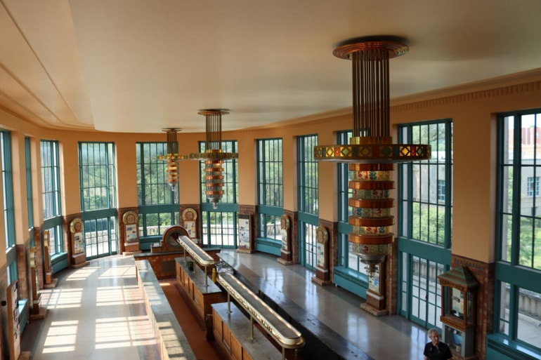 A rounded, oblong room with bluish outlined windows along the perimeter. In the middle what looks like an old school soda bar. Three light tiered and colorful light fixtures hang from the ceiling.