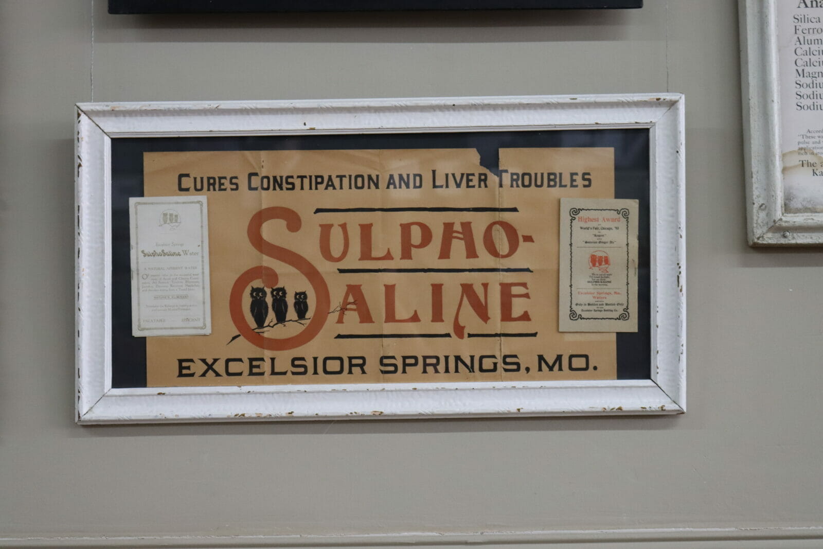 an old framed poster reads "Cures constipation and liver troubles. Sulpho-Saline Excelsior Springs, MO"