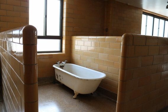 A small white painted bathtub sits next to a window, surrounded by orange tiled walls.