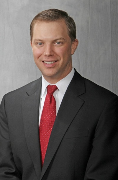 Headshot of a man in a black suit with a red tie.