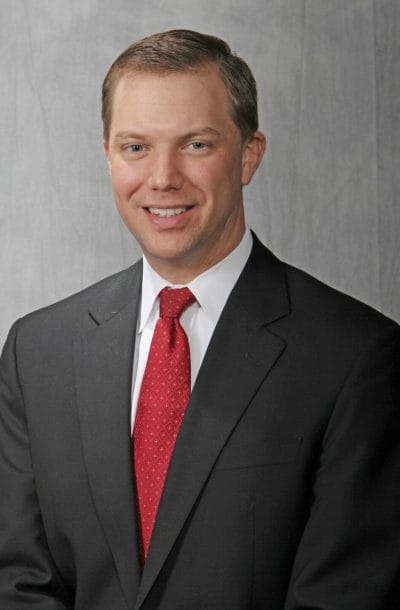 Headshot of a man in a black suit with a red tie.