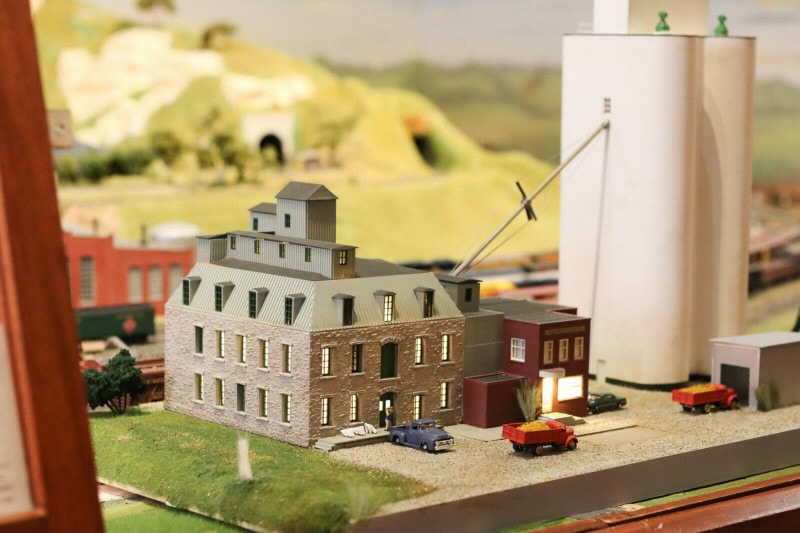 A miniature train set shows the Old Depot Museum as it would have been in the 1950s. Behind it are model train tracks and trains. A grain elevator sits next to the depot.