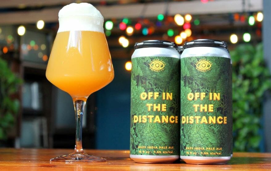 A glass and two cans of Strange Days Brewing's Off in the Distance.