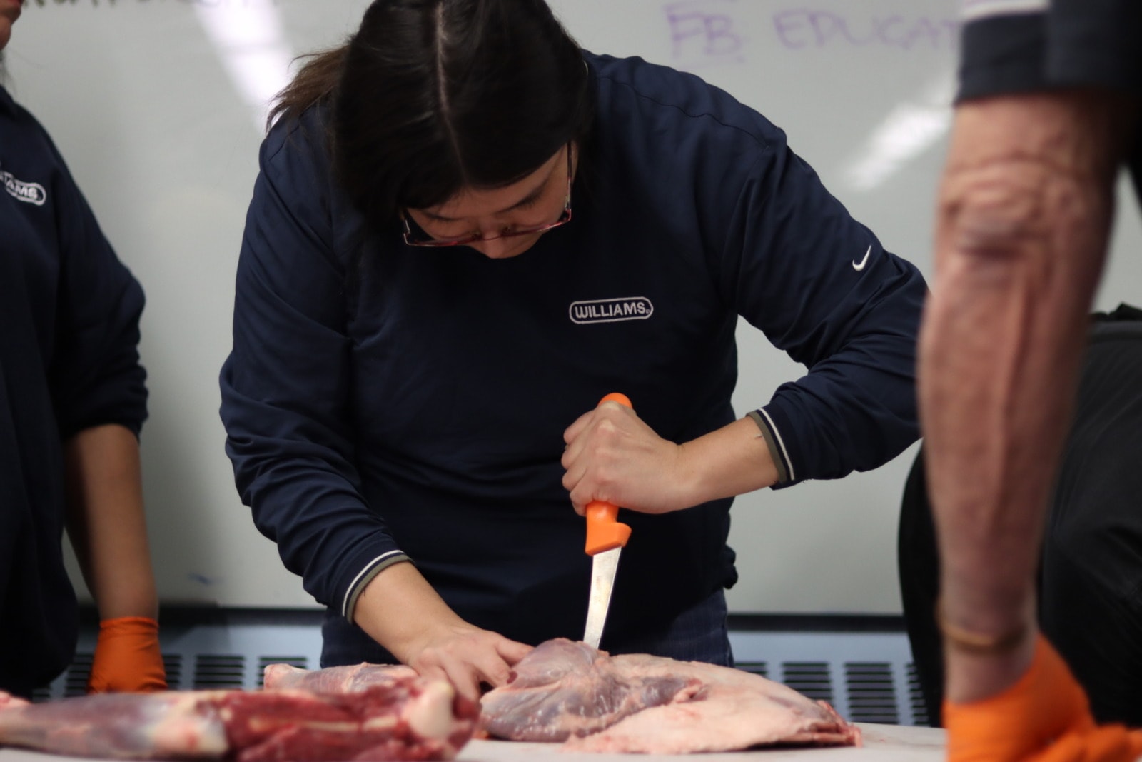 Woman holds an orange knife and separates cuts of meat on a table.