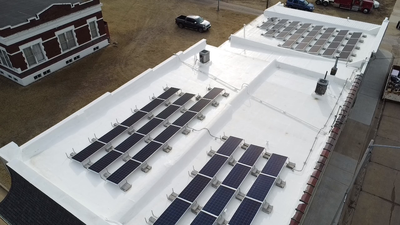Rows of solar energy panels atop a white, flat roof of a small building.