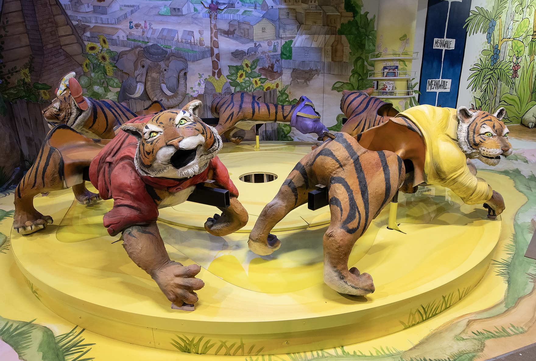 A colorful merry-go-round with tigers in an exhibit still in progress based on “Sam and the Tigers,” the book by Julius Lester. Each exhibit includes bookshelves.