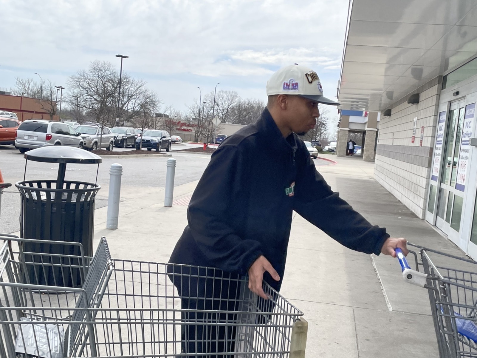 Young man pushing carts outside of a grocery store.