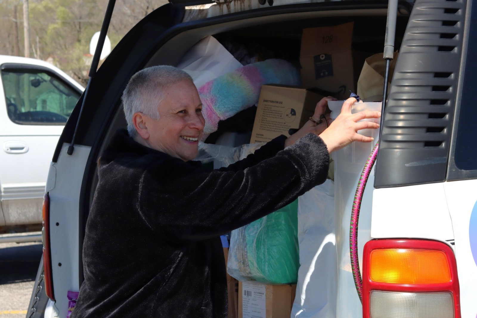 A middle-aged woman smiles while pushing a box into the back of an open SUV