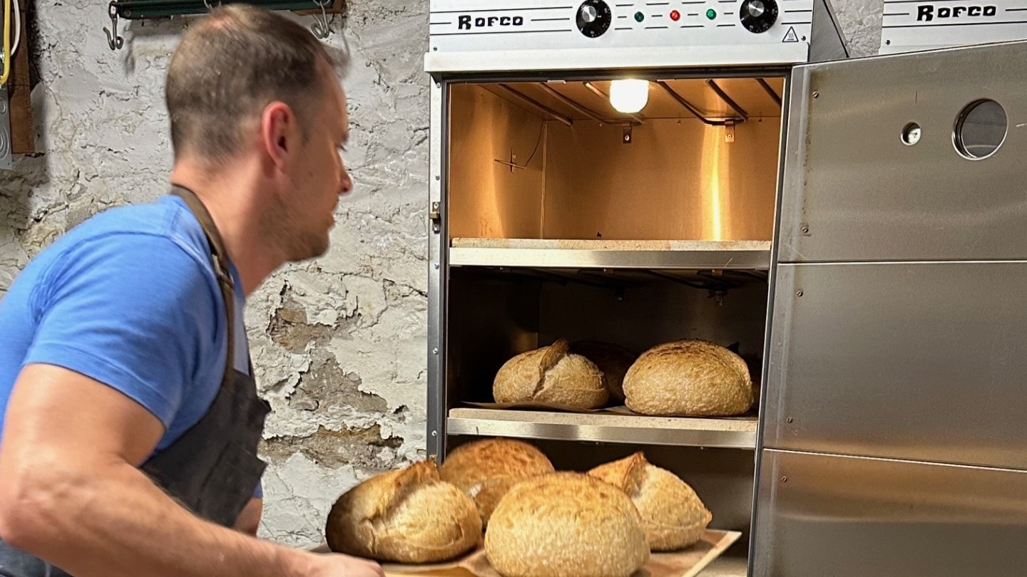 Jon Szajnuk pulls sourdough bread loaves from his oven.